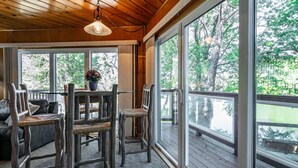 A wooden deck with a table and chairs, large windows with a view of trees, and a hanging light fixture.