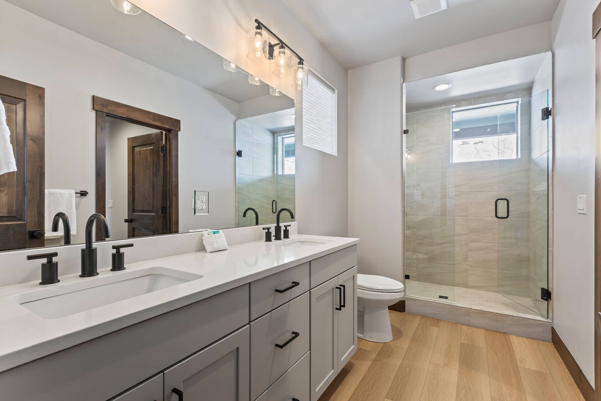 Un baño moderno con un espejo grande, dos lavamanos, un inodoro y una ducha con paredes de vidrio.