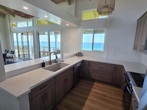 A modern kitchen with a large island, wooden cabinets, and a view of the ocean.