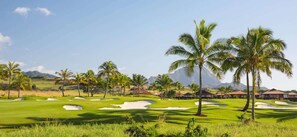 Ein Golfplatz mit Palmen, Bunkern und blauem Himmel.