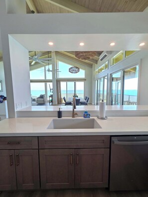 A modern kitchen with a large island, a built-in dishwasher, and a view of the ocean through large windows.