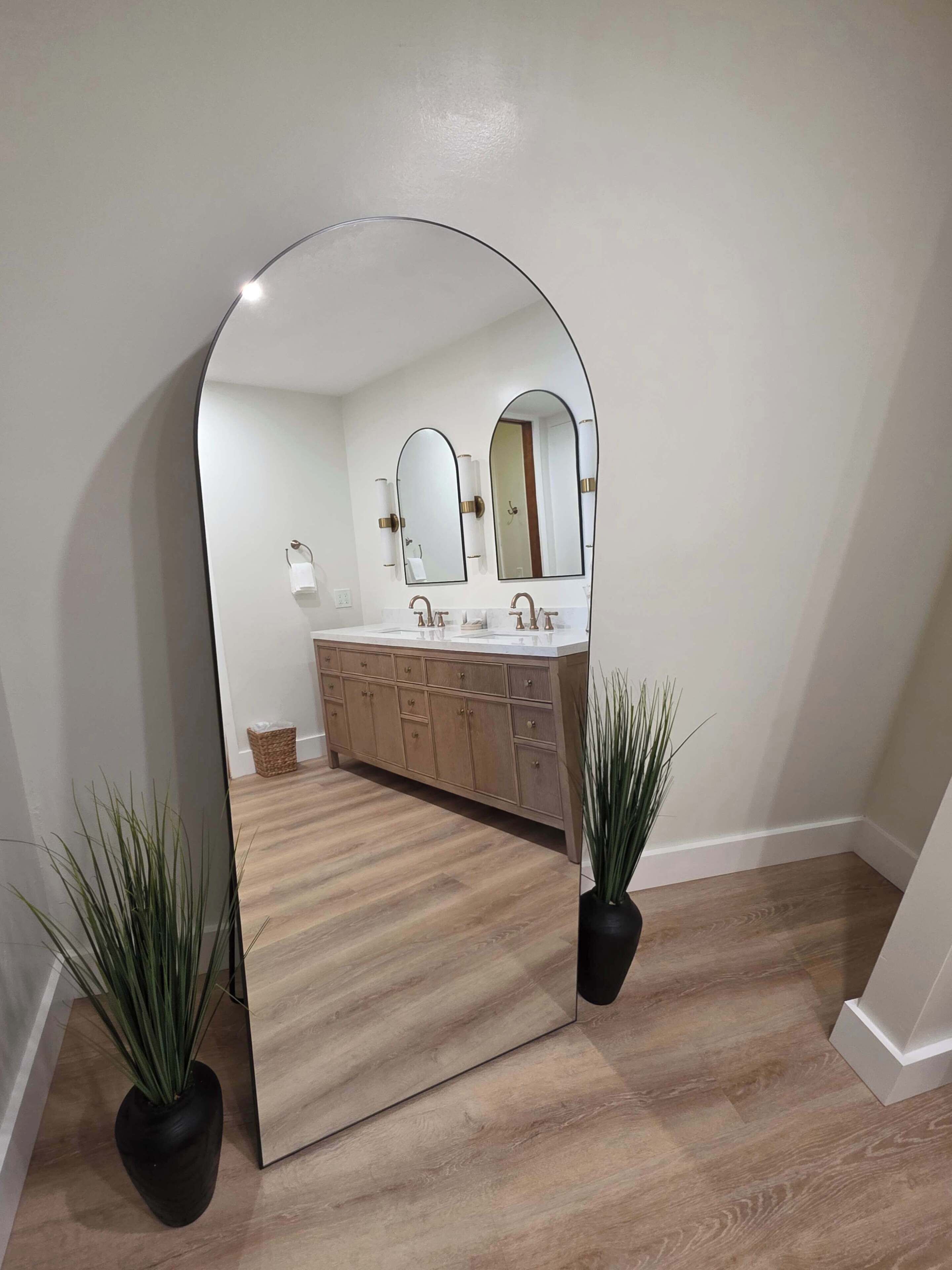 Une salle de bain avec un grand miroir, deux lavabos, des meubles en bois et deux plantes en pot.