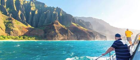 Un bateau sur des eaux turquoise, avec une côte montagneuse en arrière-plan.