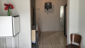 A room with a tiled floor, a television mounted on the wall, a green vase with red flowers, and a wooden chair. - HOTEL PLATINO (Sao Lourenco)