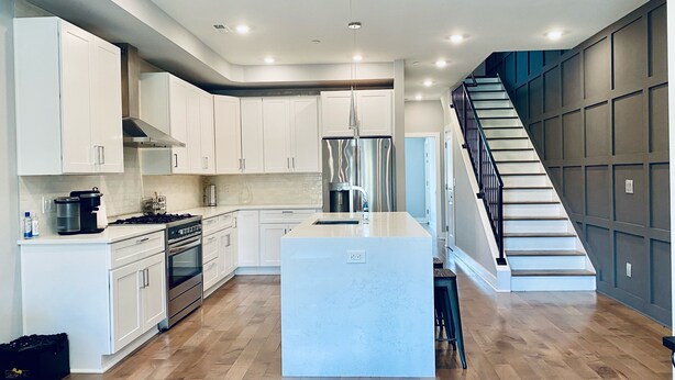 A modern kitchen with white cabinets, a central island, and a staircase to the right. - Lavish Penthouse with Private Rooftop+Views of Capitol&Monument+Parking (Washington)