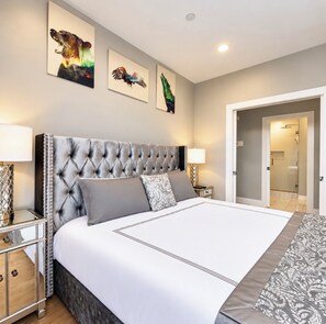 A bedroom with a tufted headboard, a large bed with grey bedding, two bedside tables with lamps, and three wall-mounted artworks. - Lavish Penthouse with Private Rooftop+Views of Capitol&Monument+Parking (Washington)