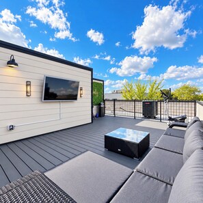 A rooftop deck with a flat-screen TV, outdoor seating, and a view of the sky.