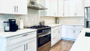 A modern kitchen with white cabinets, stainless steel appliances, and a wooden floor. - Lavish Penthouse with Private Rooftop+Views of Capitol&Monument+Parking (Washington)