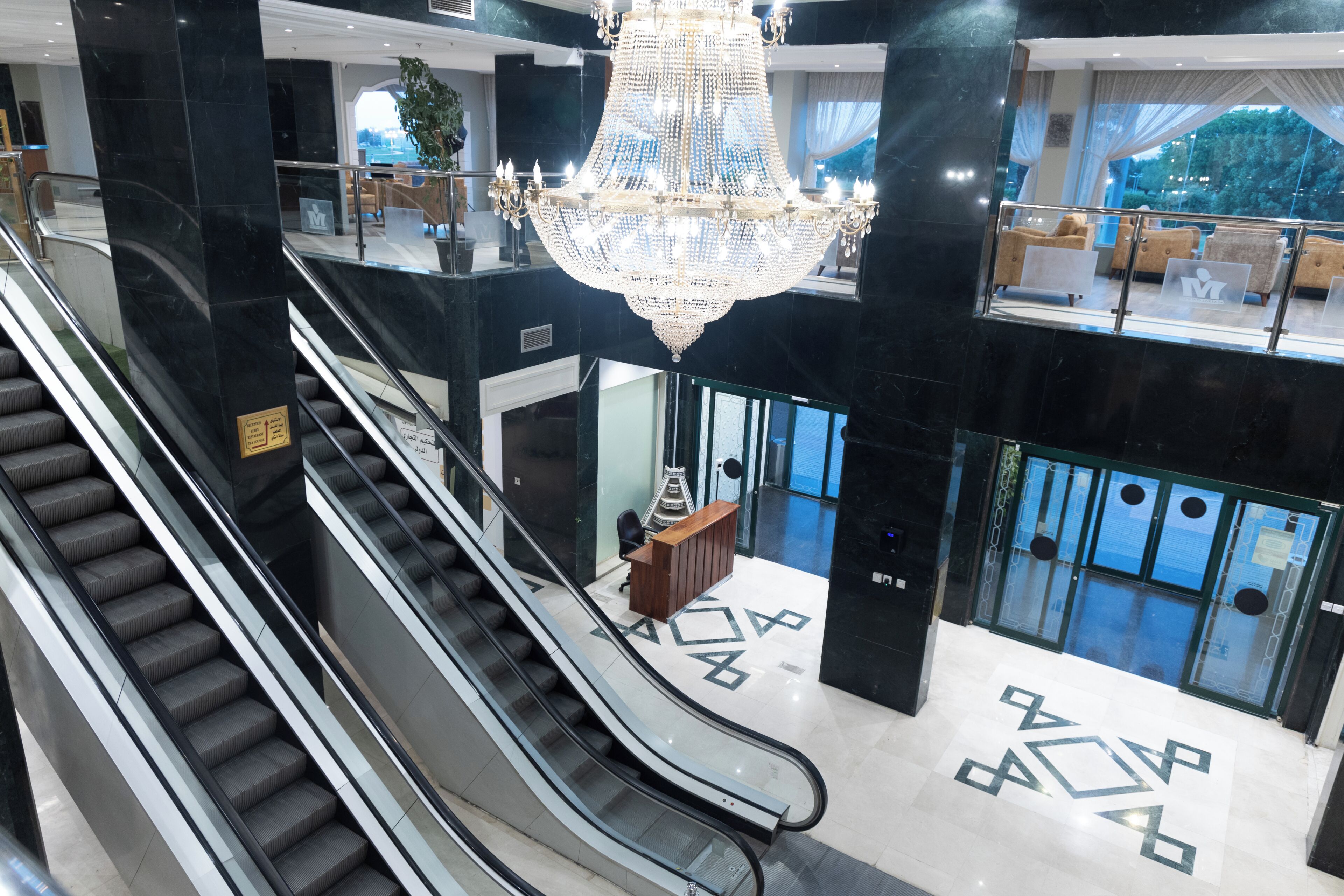 An indoor area with escalators, a reception desk, and a chandelier.
