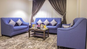 A living room with two blue sofas, a coffee table with decorative items, and a large window with curtains. - Garden View Hotel (Tabuk)