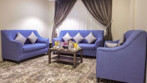 A living room with two blue sofas, a coffee table with decorative items, and a large window with curtains. - Garden View Hotel (Tabuk)