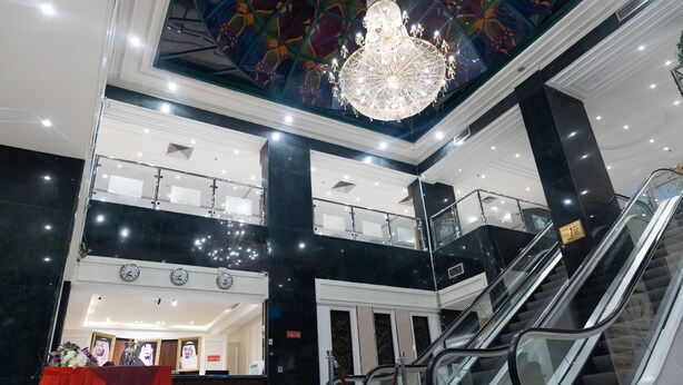 A lobby with a chandelier, escalators, and a red curtain. - Garden View Hotel (Tabuk)