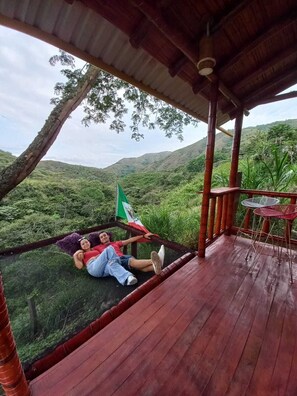 A wooden deck with a hammock and a flag, overlooking a lush green landscape.