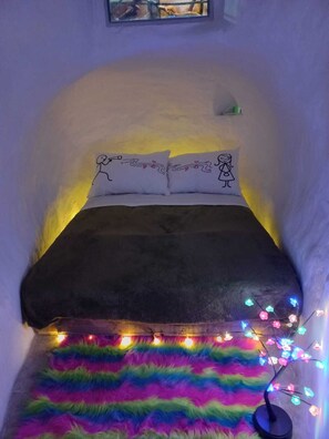 A small, cozy room with a bed, a fluffy rug, and string lights.