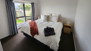 Un dormitorio con una cama grande, una ventana con cortinas, una mesita de noche con lámpara y vistas al exterior.