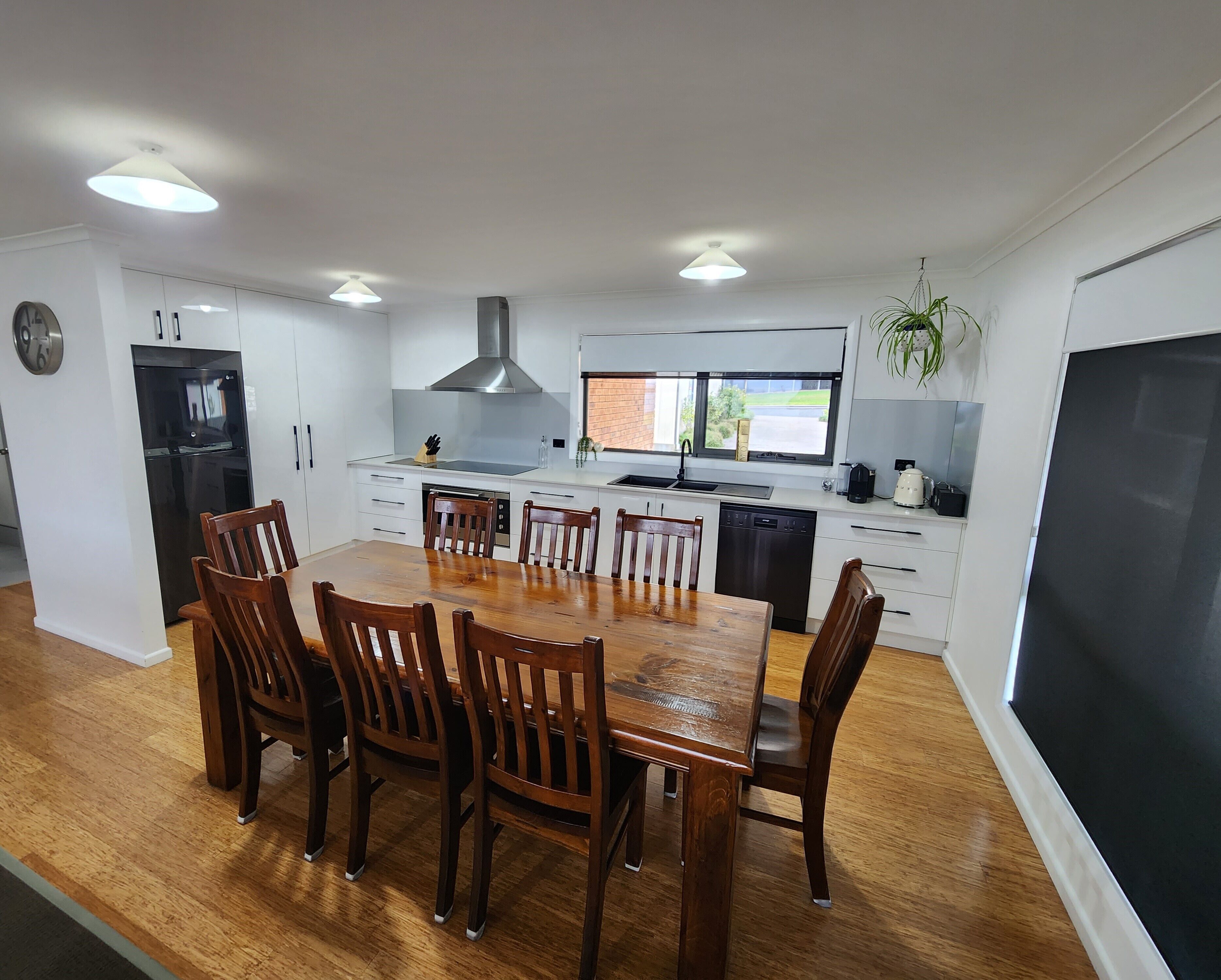 A modern kitchen with white cabinets, a black refrigerator, a stainless steel range hood, and a dining area with wooden chairs and a large table.
