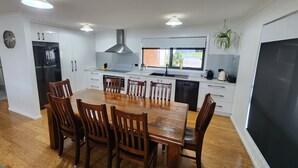 Una cocina moderna con armarios blancos, un refrigerador negro, una campana extractora de acero inoxidable y un comedor con sillas de madera y una mesa grande.