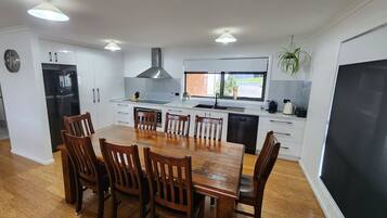 A modern kitchen with white cabinets, a black refrigerator, a stainless steel range hood, and a dining area with wooden chairs and a large table.
