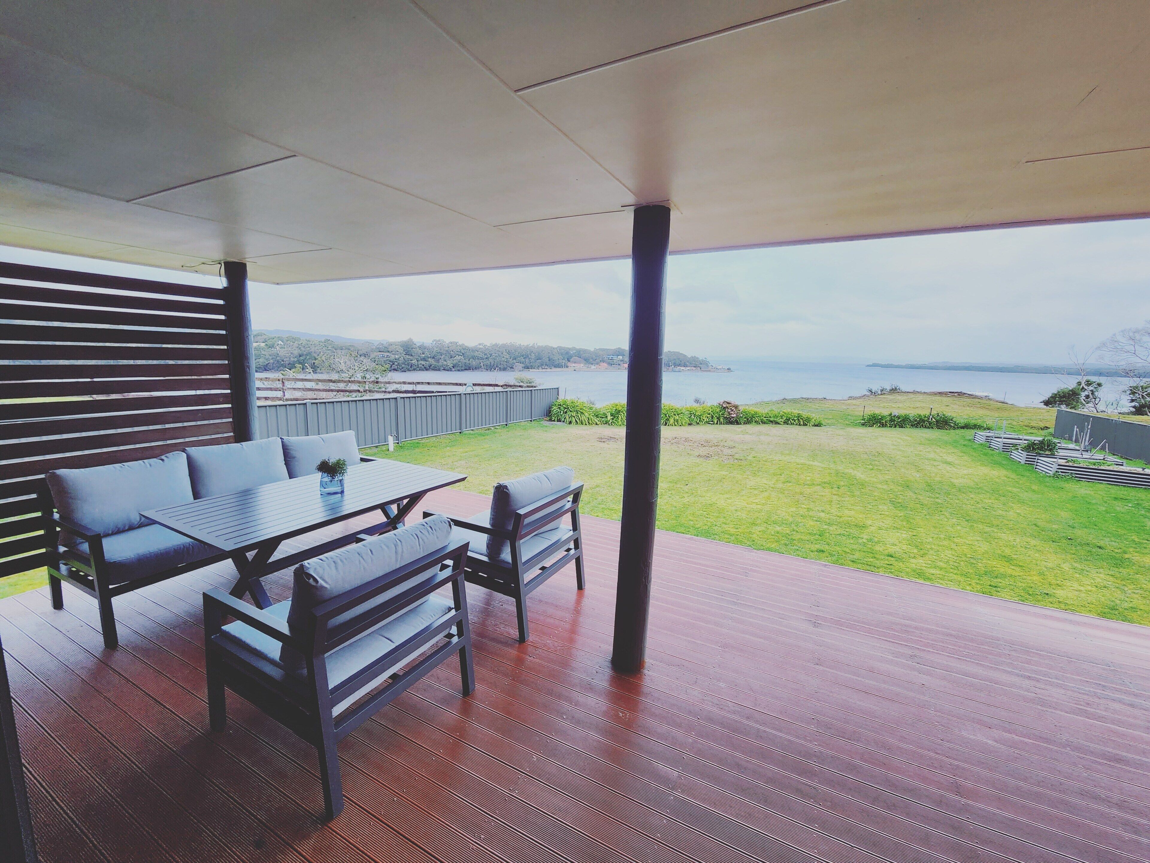 A covered patio with a table and chairs, overlooking a grassy area and a body of water.
