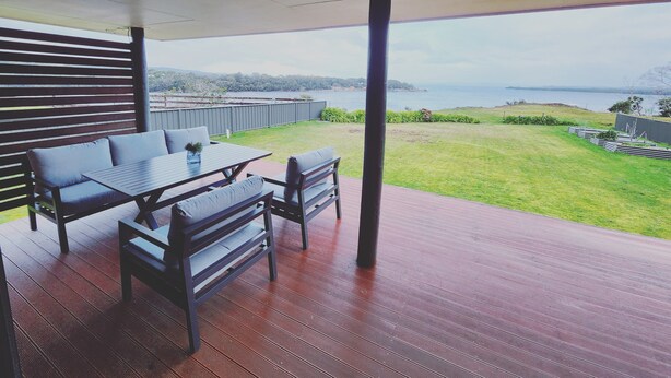Un patio techado con una mesa y sillas, con vista a un área verde y una masa de agua.
