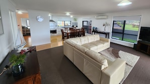 Una sala de estar moderna con un sofá color beige, un comedor con sillas de madera y una cocina al fondo.