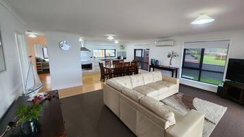 A modern living room with a beige sofa, a dining area with wooden chairs, and a kitchen in the background.