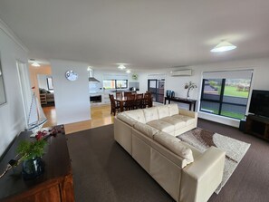 A modern living room with a beige sofa, a dining area with wooden chairs, and a kitchen in the background. - Spectacular views of Macquarie Harbour from your very own private deck! (Strahan)