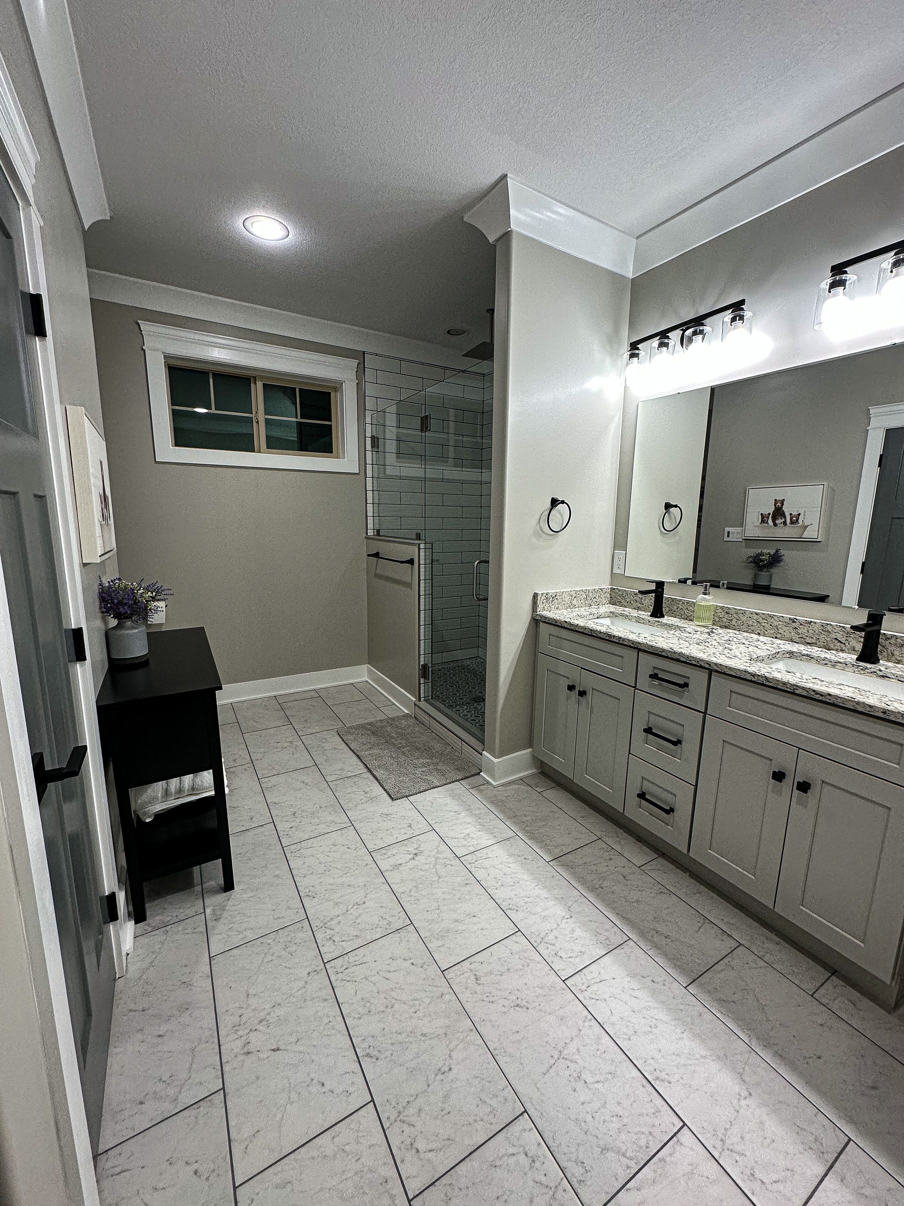 A modern bathroom with a walk-in shower, a vanity with a mirror, and a small table with a plant.