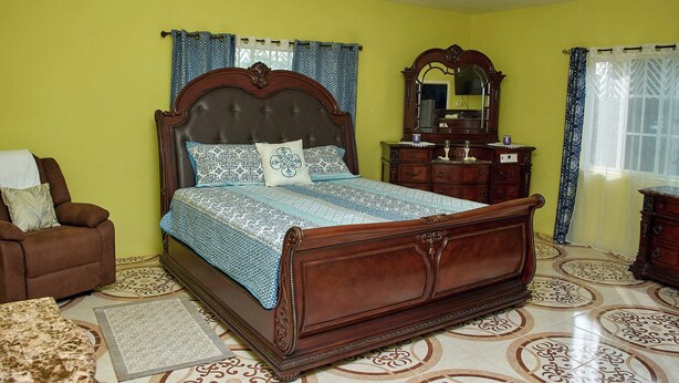 Een slaapkamer met een groot bed, een stoel, een dressoir en een spiegel.
