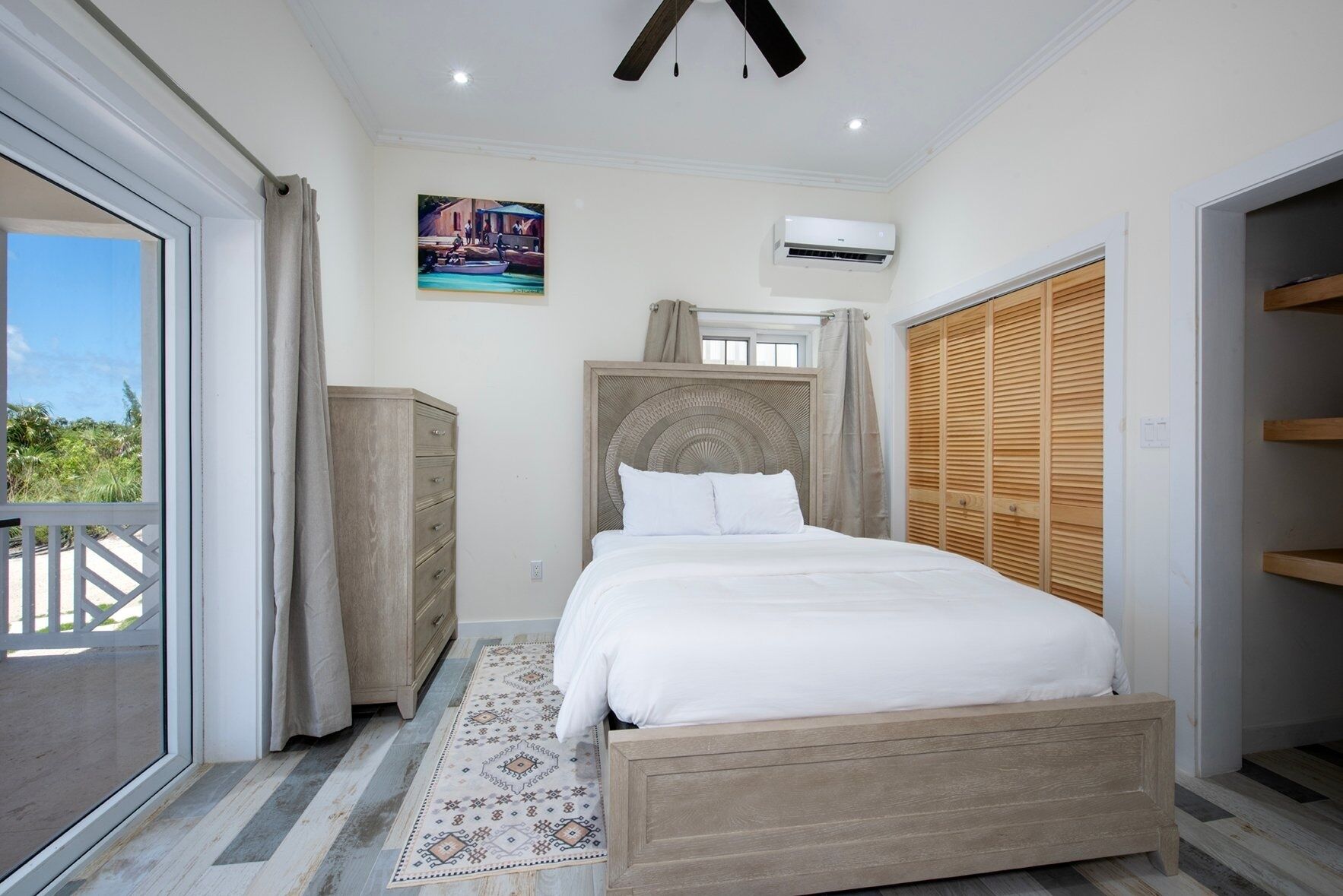 A bedroom with a bed, a dresser, a ceiling fan, an air conditioning unit, and a window with a view of greenery.