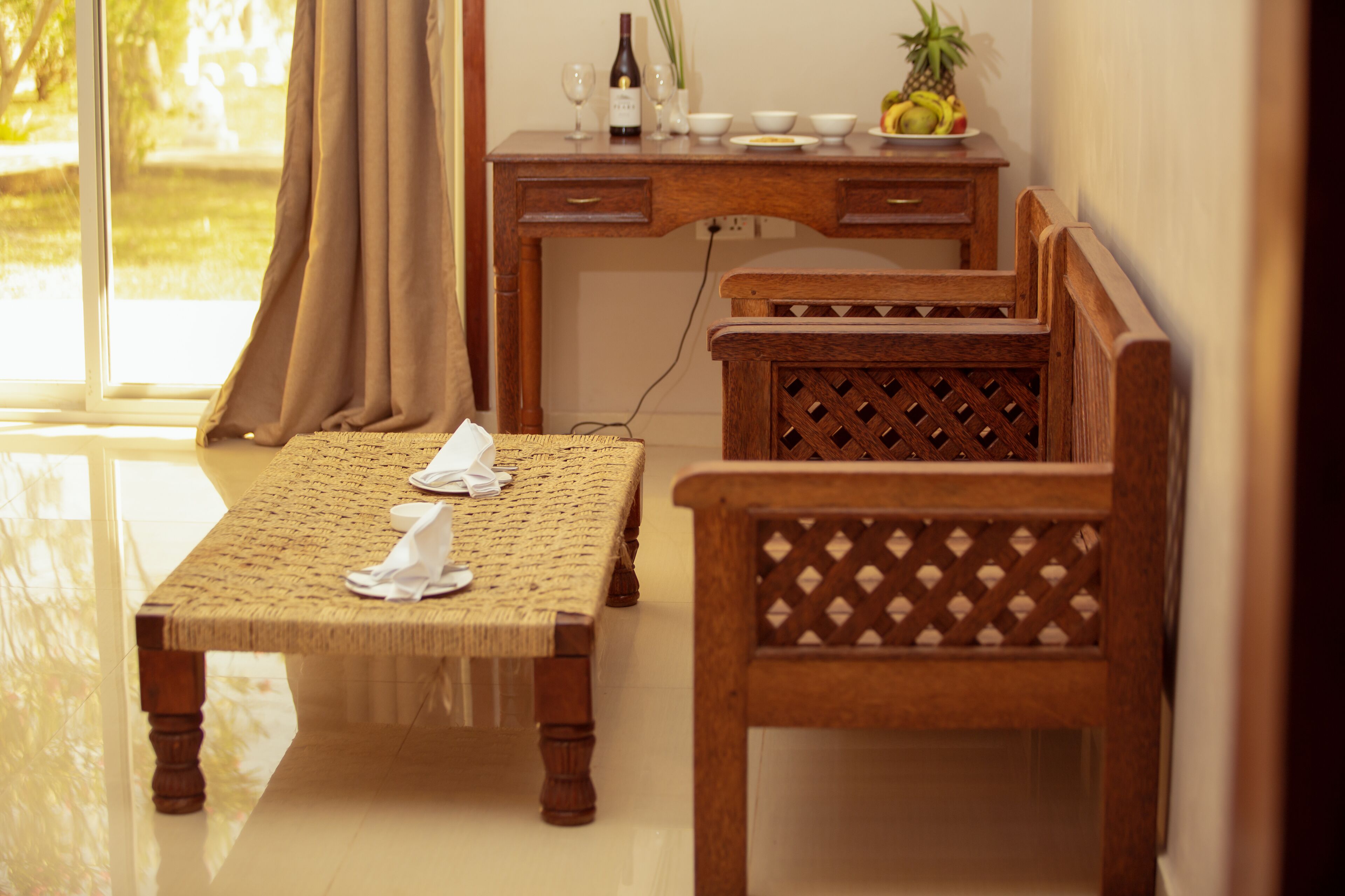 Ein Zimmer mit einem Holztisch, gedeckt für zwei Personen, einer Holzbank, einem Schreibtisch mit Flasche und Gläsern und Blick auf Grünflächen.