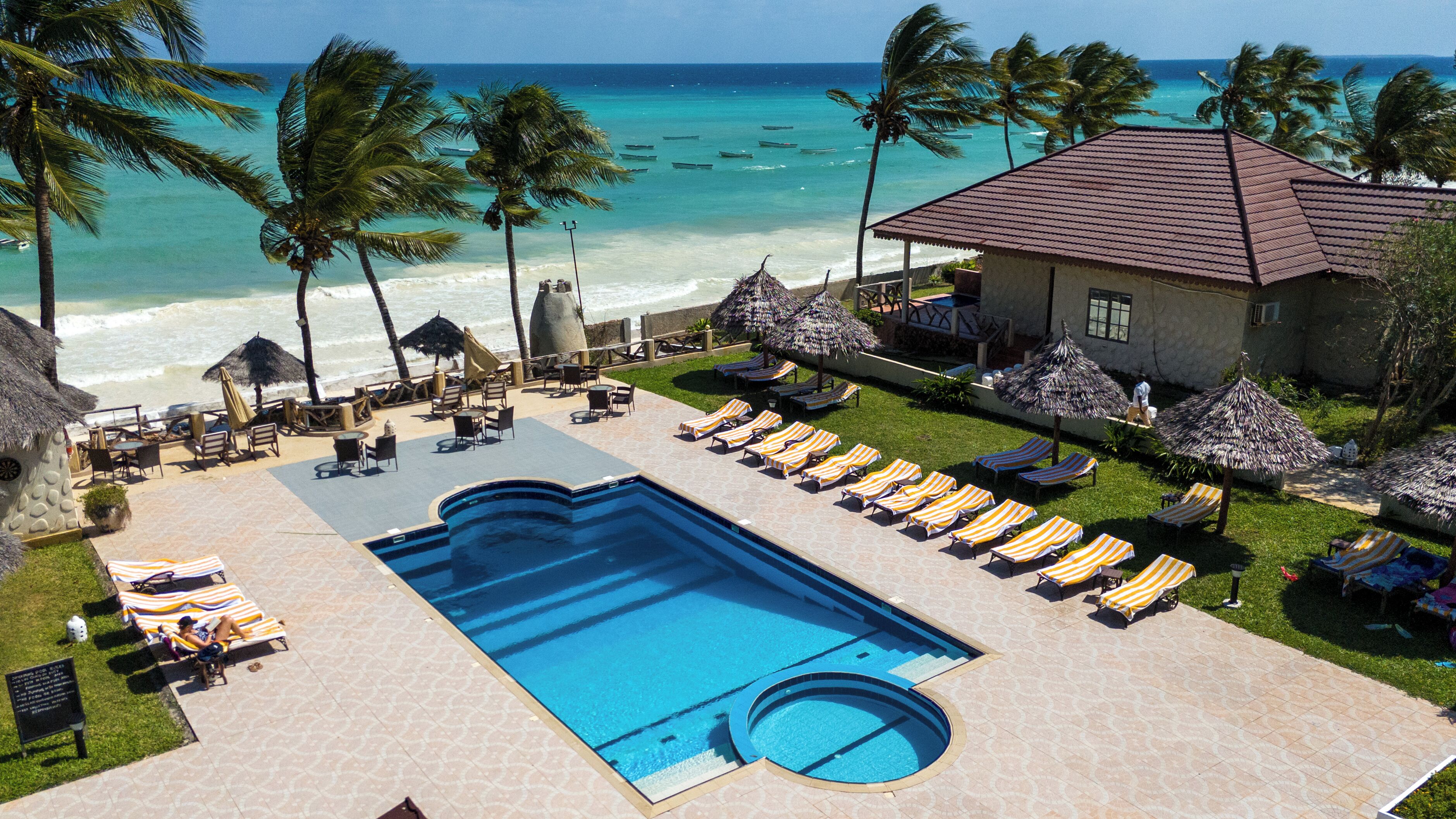 A pool area with lounge chairs and umbrellas, a building with a red roof, and a view of the ocean.