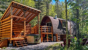 A rustic cabin with a wooden deck, a covered porch, and a chimney.