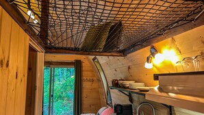 A cozy cabin interior with a wooden ceiling, a dining area with a sink, and a window offering a view of greenery.