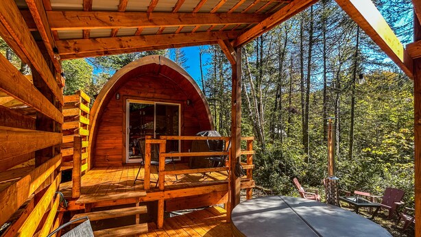 A wooden cabin with a hot tub, a covered deck, and a view of the forest.