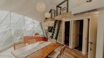 Ein Zimmer mit großem Fenster, einem Holztisch und einer Treppe zu einer oberen Ebene.