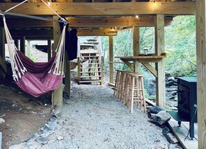 A rustic wooden structure with a hammock, a wooden ladder, and a grill.