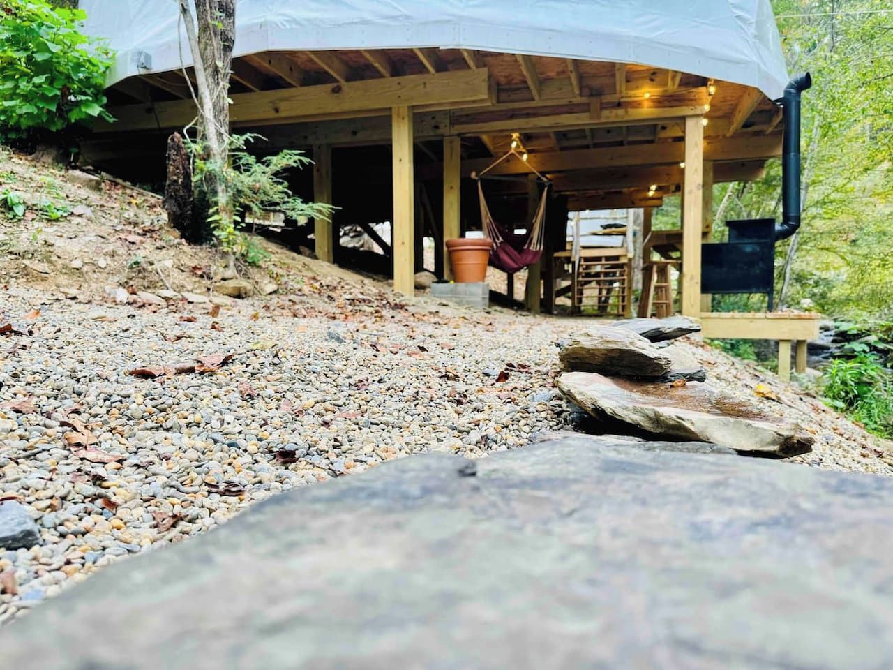 A wooden cabin with a covered porch, a hanging hammock, and a rustic outdoor setting.