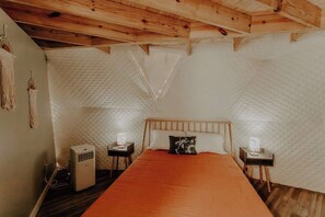 A bedroom with a wooden ceiling, a bed with an orange bedspread, two bedside tables with lamps, and a wall-mounted air conditioner.