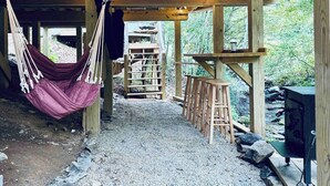 Une structure rustique en bois, dotée d’un hamac, de tabourets en bois et d’un espace barbecue.