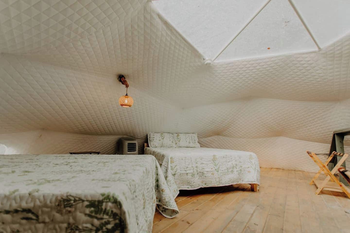 Une chambre mansardée chaleureuse avec un plafond en pente, deux lits avec une literie à motifs floraux, un luminaire suspendu et une échelle en bois.