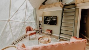Un salon moderne doté d’une grande fenêtre, d’un téléviseur et d’un espace en mezzanine.