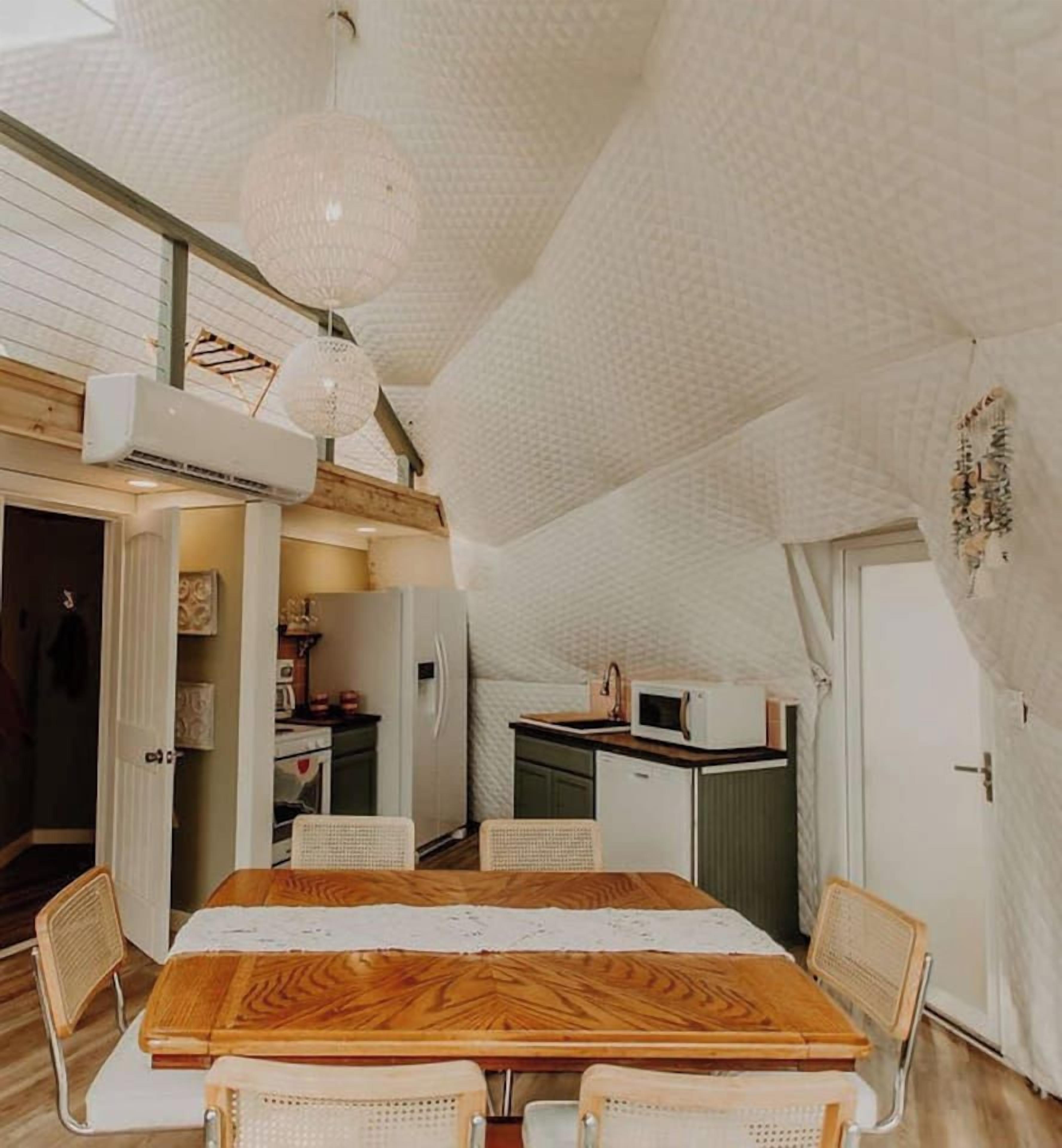 Zona pranzo con tavolo e sedie in legno, una cucina sullo sfondo e un soffitto strutturato.