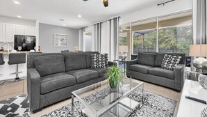 A modern living room with two grey sofas, a glass coffee table, and a ceiling fan.