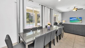 A modern dining area with a glass table, grey chairs, and a vase of flowers.