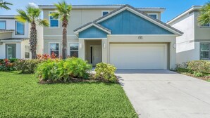 A two-story residential building with a garage, surrounded by well-maintained lawns and palm trees.