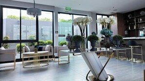Un moderno vestíbulo de hotel con ventanas amplias, una mesa de recepción y zonas de estar.