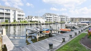 A marina with docked boats, a wooden dock, and residential buildings in the background.