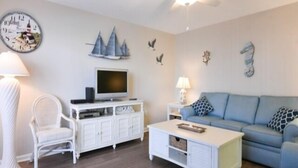 A living room with a white TV stand, a blue sofa, a white coffee table, a white chair, and a ceiling fan.