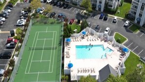 An aerial view of a property with a tennis court, a swimming pool, and a parking lot.